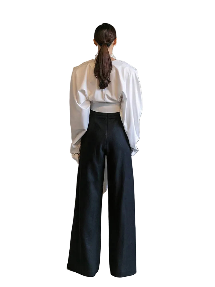 Back view of a white draped long-sleeve wrap top with a fitted waist, worn with black pants.
