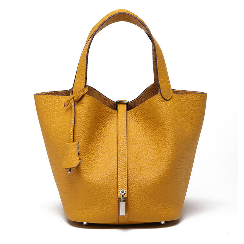 Mustard yellow pebbled bucket bag with twin handles, a front strap, padlock, and hanging tag, front view.