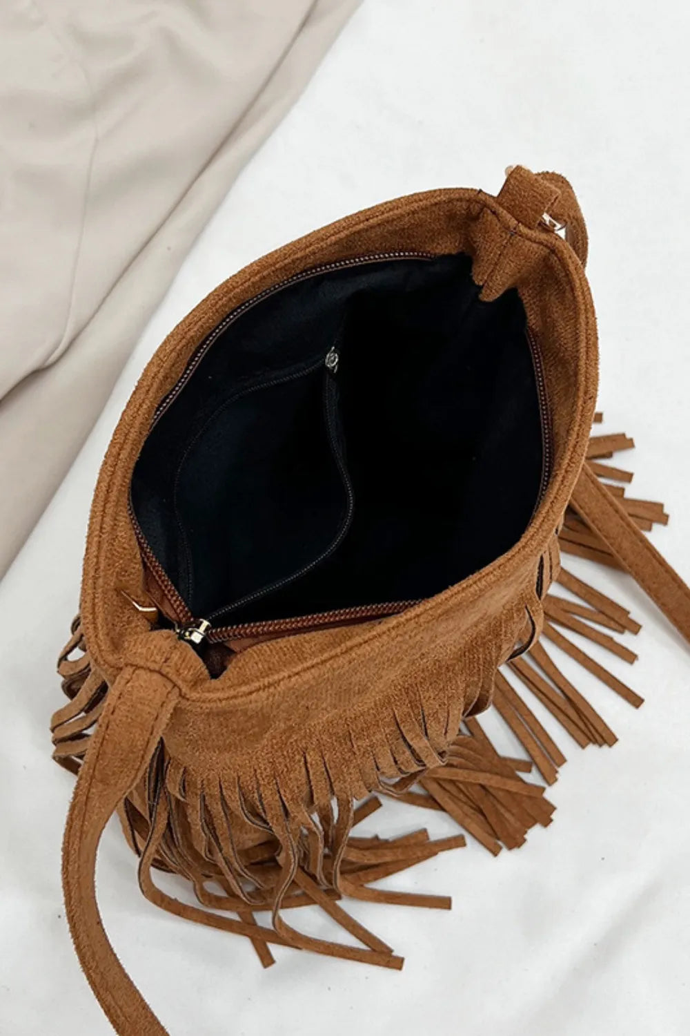 Top-down view inside a tan fringe bag showing black lining, an inner pocket, and a zippered opening.