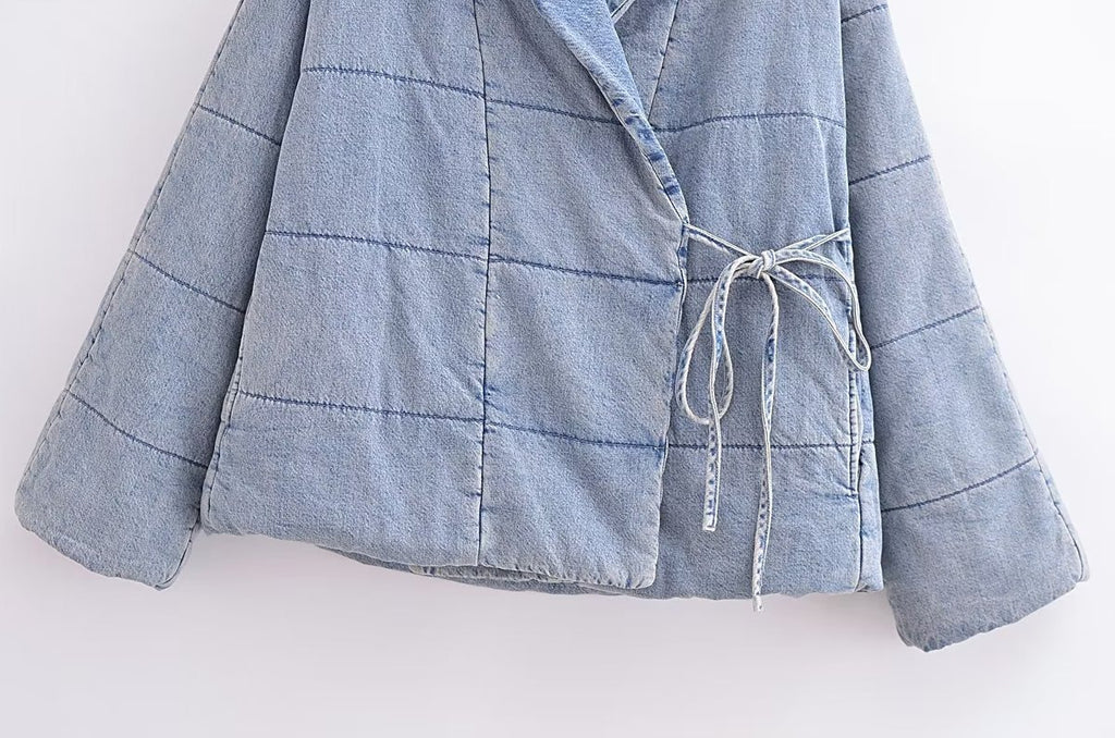 Close-up of the light blue quilted jacket's side ties, patch pocket, and stitched hem.