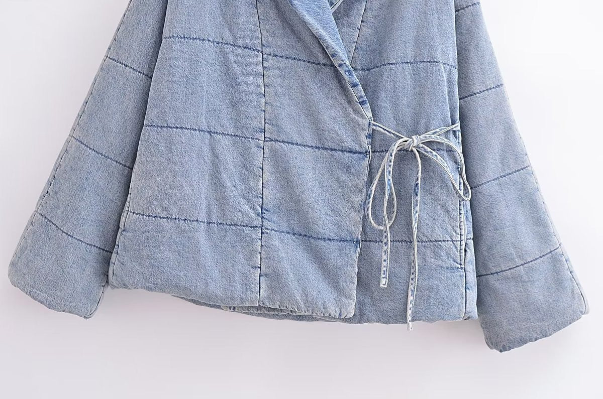 Close-up of the light blue quilted jacket's side ties, patch pocket, and stitched hem.