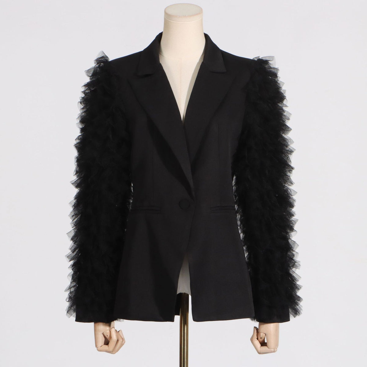 Black tailored blazer with layered tulle ruffles down the sleeves on a mannequin, front view.