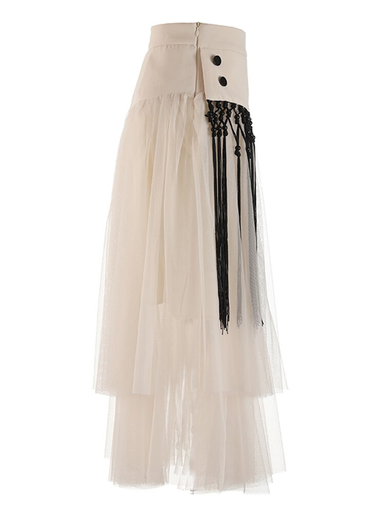 Side view of a cream layered mesh skirt showing a zipper, two black buttons, and long black fringe.