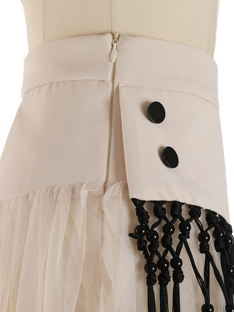 Close-up of the zipper, black buttons, and knotted fringe on a cream layered mesh skirt.