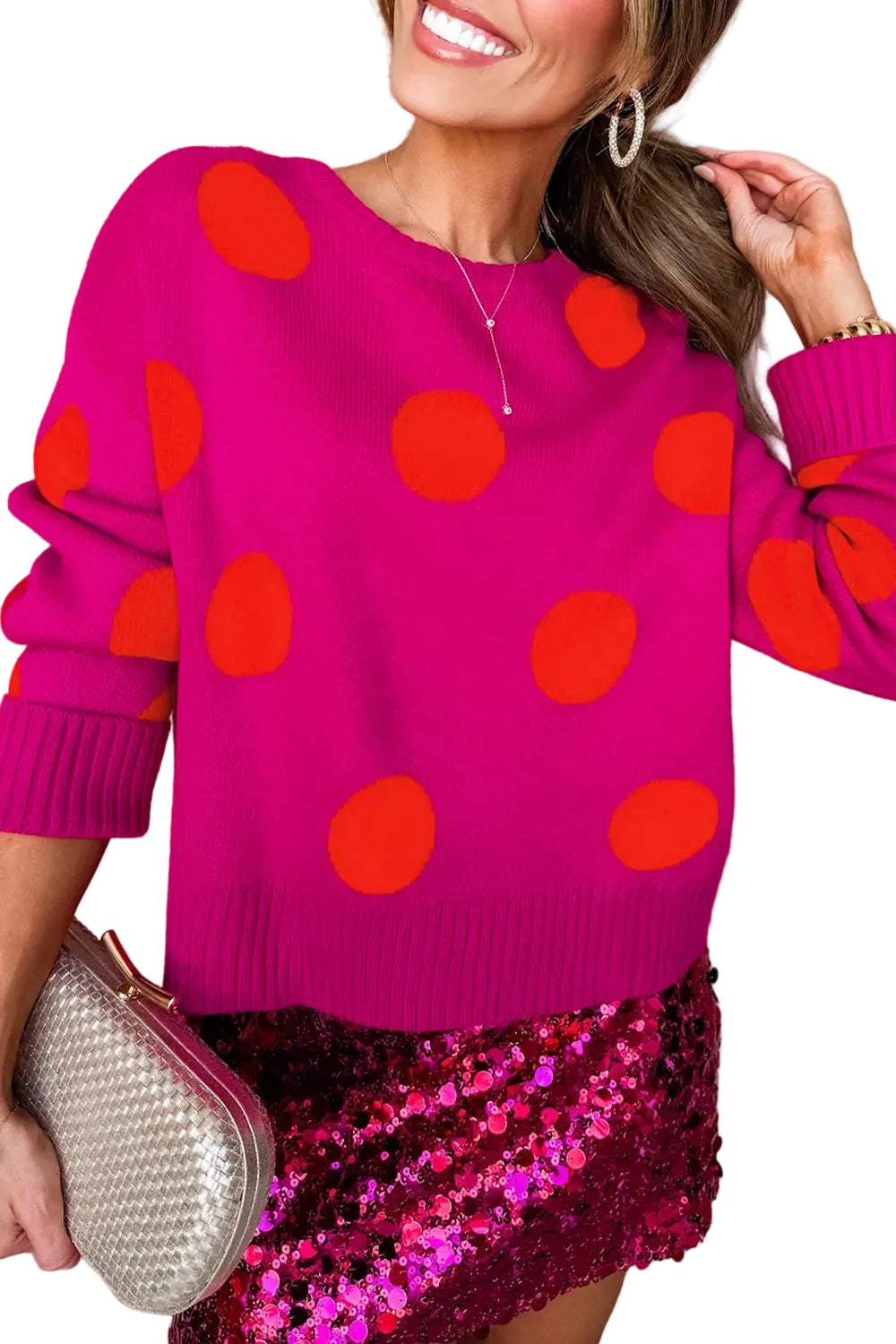 Angled front view of a bright pink crewneck sweater with oversized orange polka dots and ribbed cuffs.