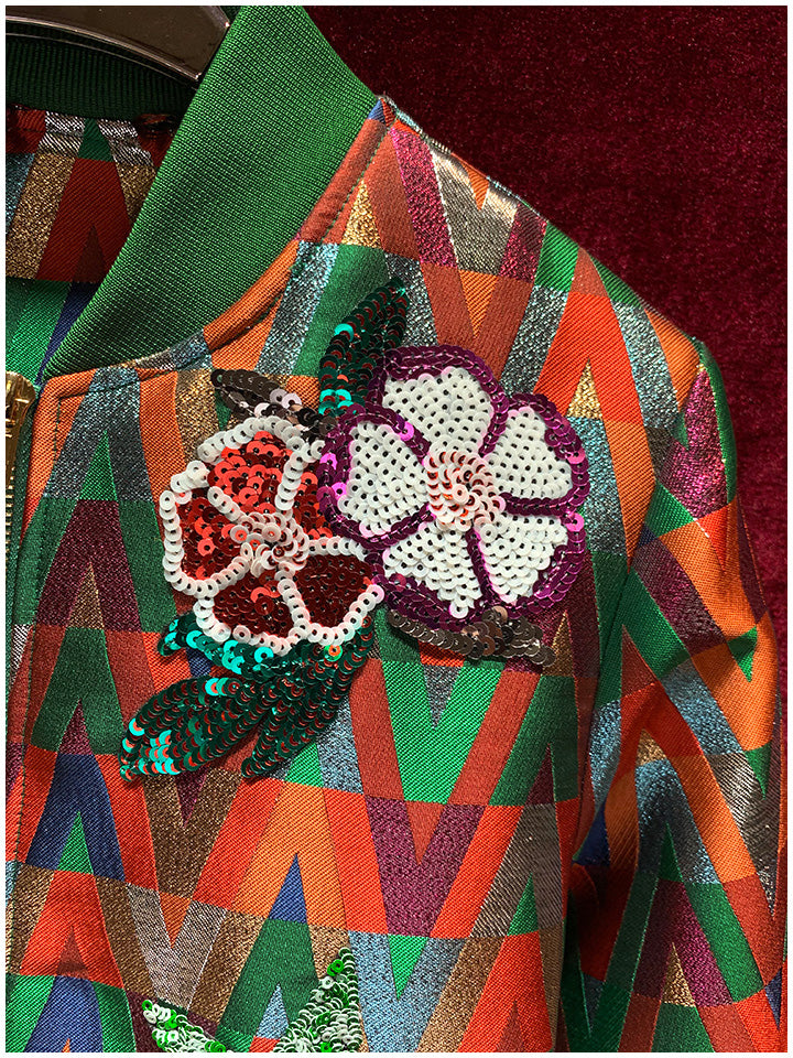 Close-up of sequin flower patches on the bomber jacket's multicolor geometric fabric.
