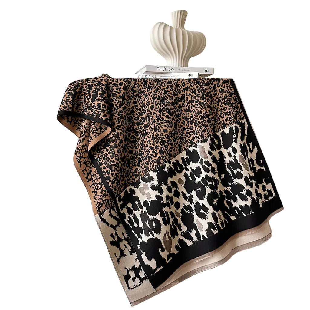 Beige and black mixed-scale leopard-print scarf spread over a chair, showing its border and short fringe.