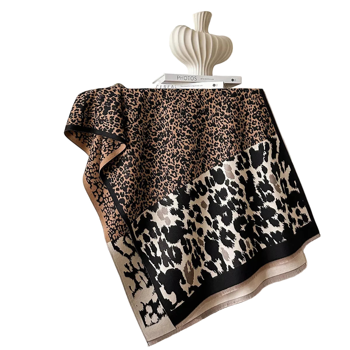 Beige and black mixed-scale leopard-print scarf spread over a chair, showing its border and short fringe.
