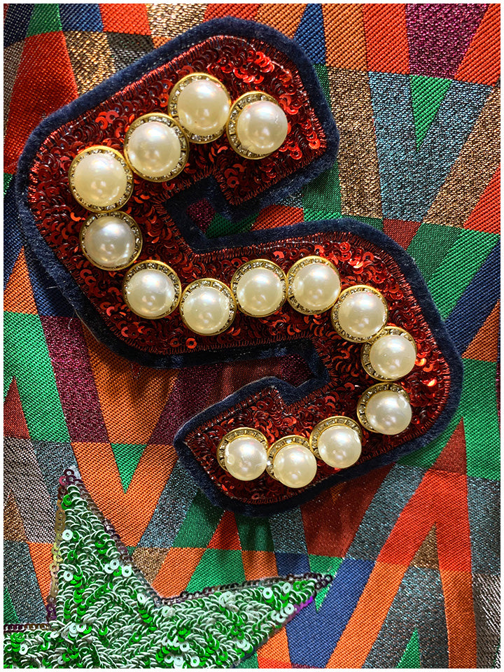 Close-up of the bomber jacket's red sequin S patch with pearl-like beads on multicolor geometric fabric.