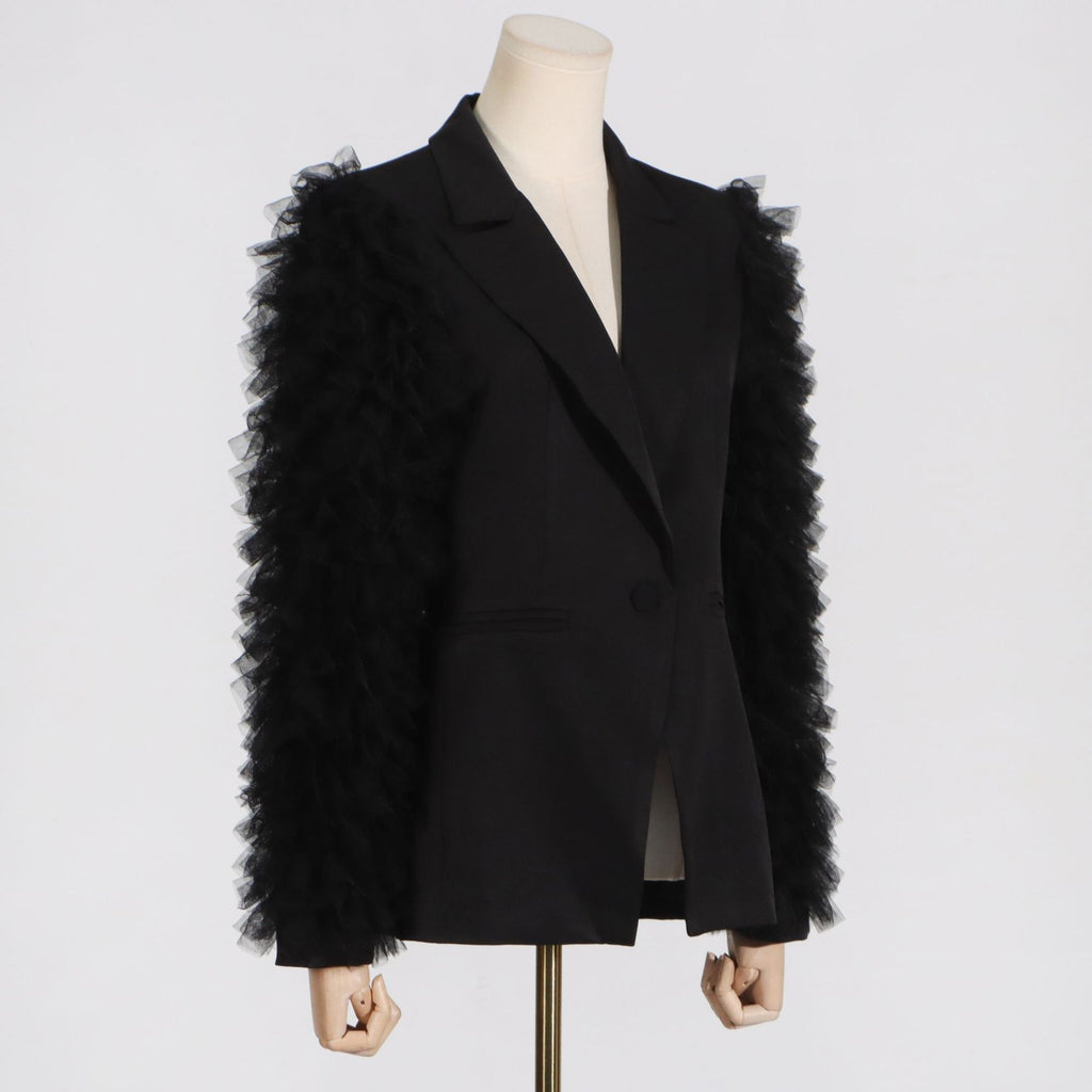 Angled view of a black tailored blazer with layered tulle sleeve ruffles on a mannequin.