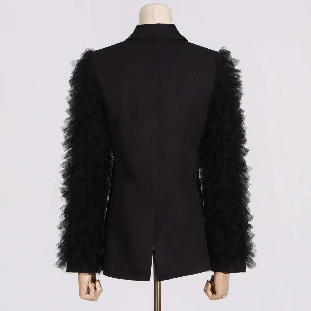 Back view of a black tailored blazer with layered tulle sleeve ruffles and a center vent.