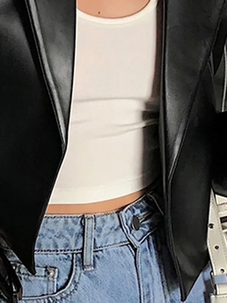 Close-up of a black shiny cropped jacket's lapels and hem, worn with a white top and blue jeans.