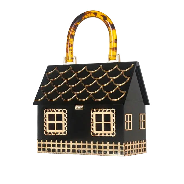 Black house-shaped handbag with gold window and fence details and an amber patterned handle, angled view.