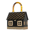 Black house-shaped handbag with gold window and fence details and an amber patterned handle, angled view.