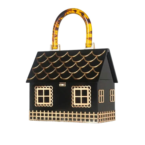 Black house-shaped handbag with gold window and fence details and an amber patterned handle, angled view.