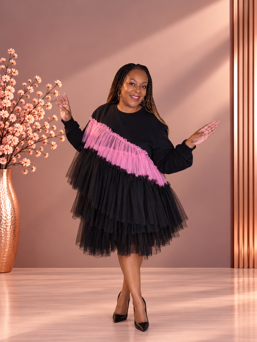 Model wearing a black long-sleeve dress with asymmetric pink and black tiered tulle ruffles, front view.