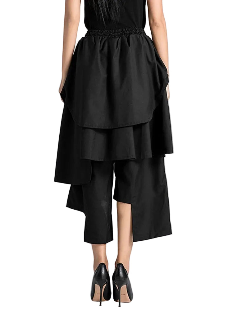 Back view of black cropped wide-leg pants with layered asymmetric panels and an elastic waist.