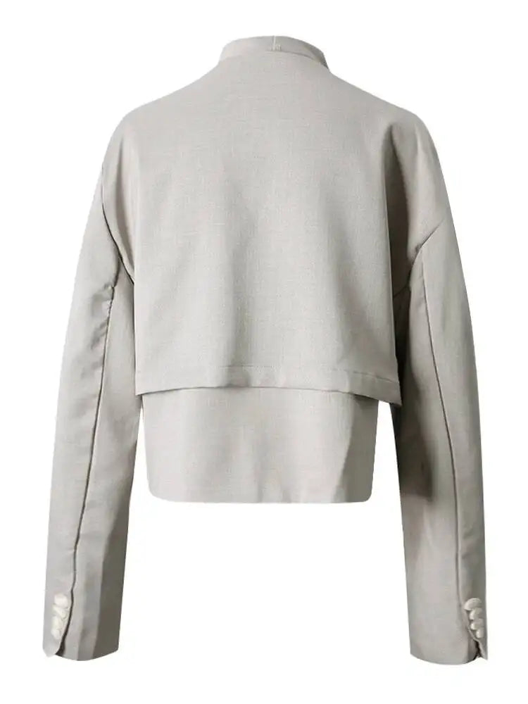Back view of a light gray cropped jacket with a layered hem, dark piping, and cuff buttons.