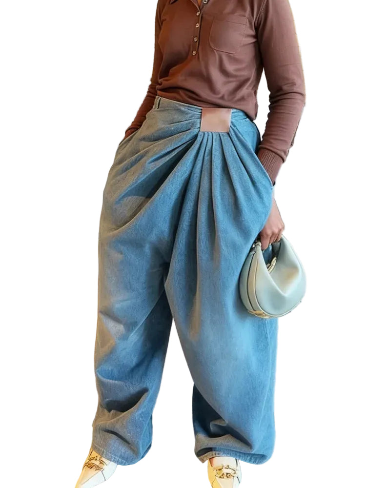 Angled view of blue wide-leg jeans showing gathered front pleats and a rectangular brown waist patch.