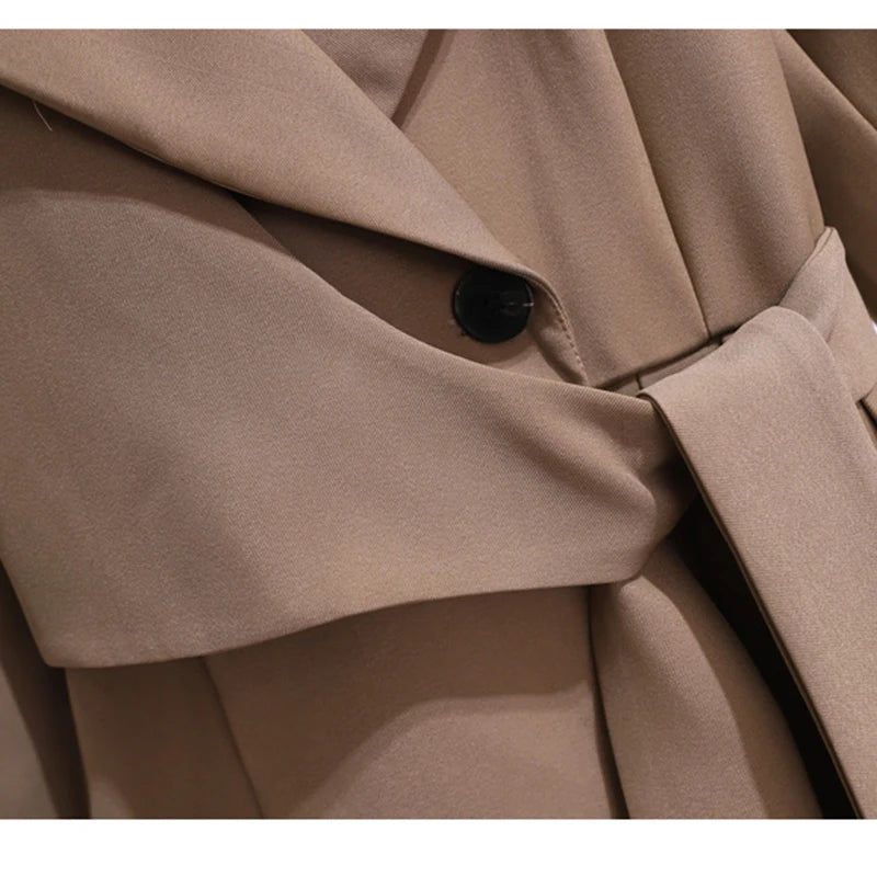 Close-up of a taupe blazer-style dress's waist button, sleeve-like tie, and pleated skirt.
