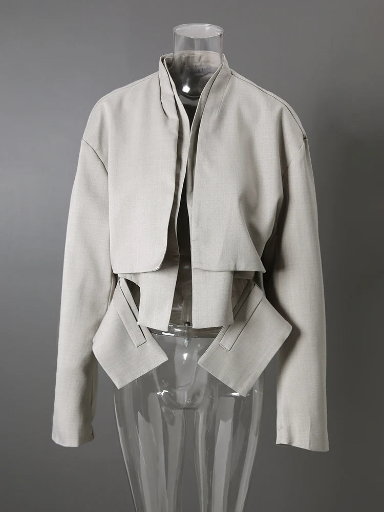 Light gray cropped jacket with angular hanging front panels and dark piping on a clear mannequin, front view.