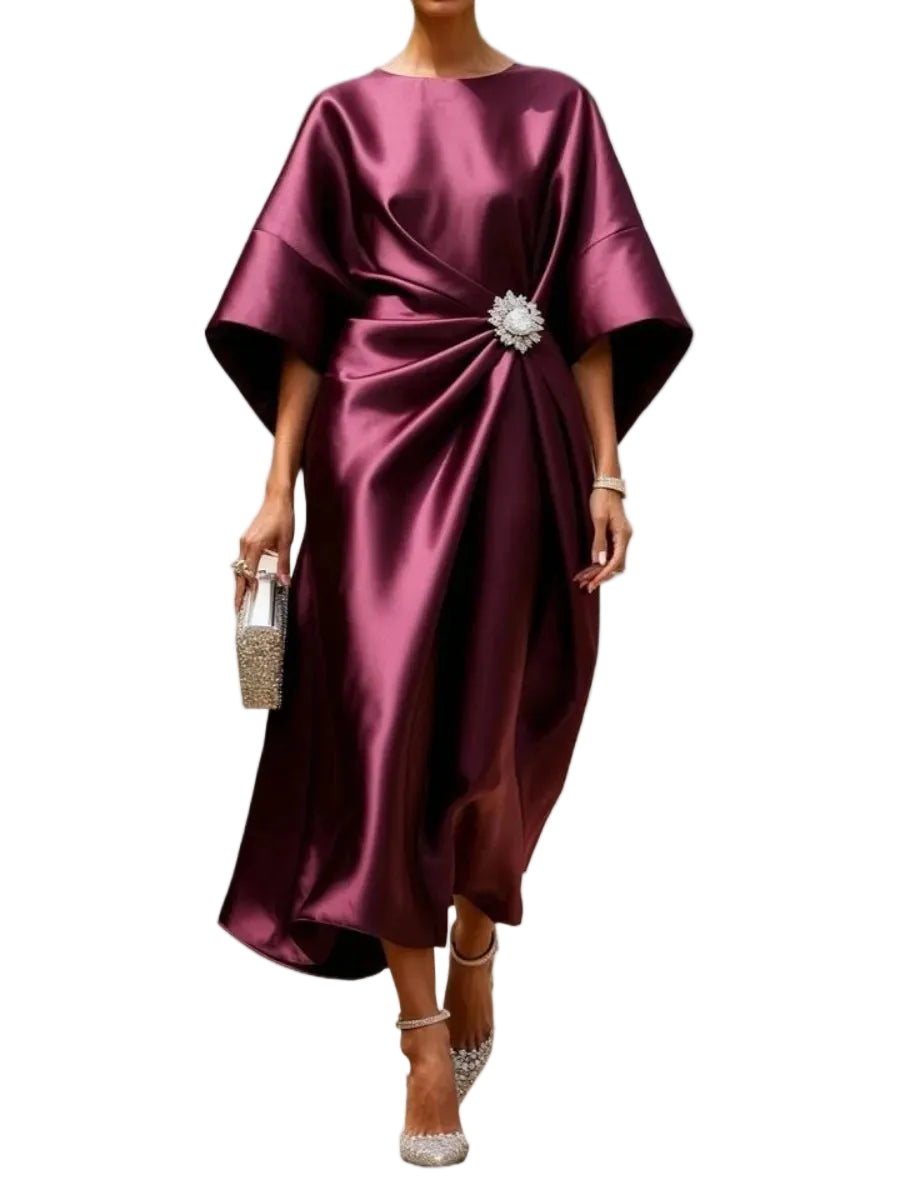 Model wearing a burgundy satin-look draped midi dress with wide sleeves and a sparkling waist brooch, front view.