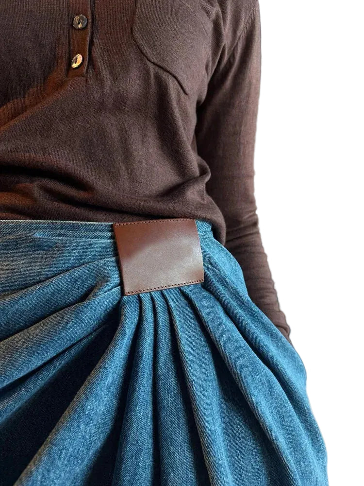 Close-up of gathered denim pleats and a rectangular brown patch at the front waist.