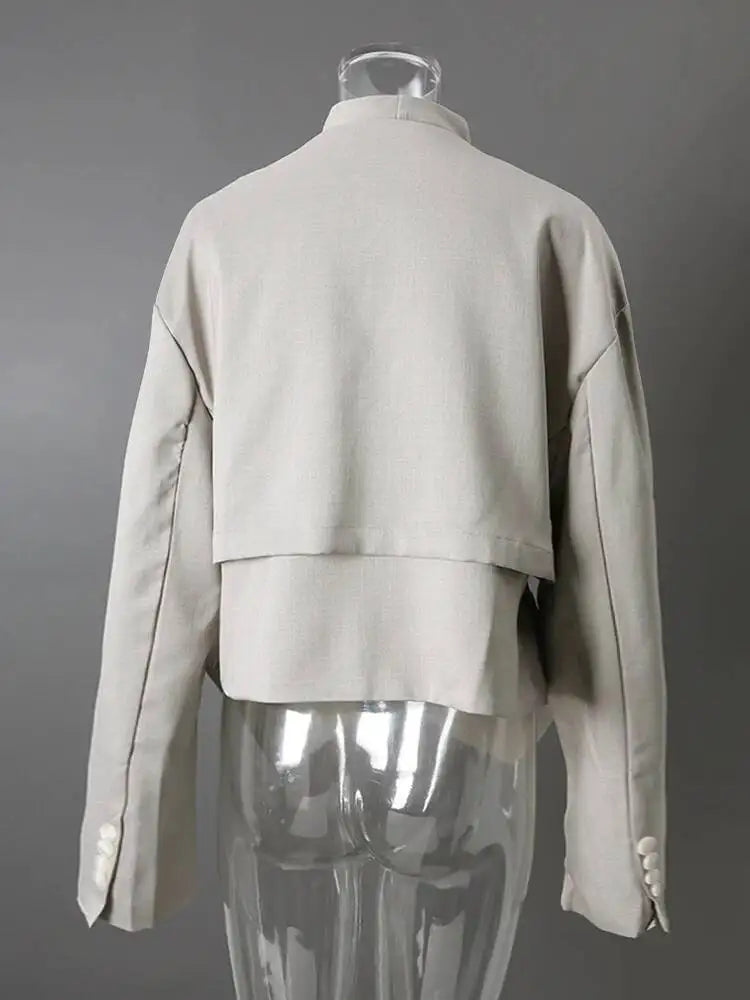 Back view of a light gray layered cropped jacket on a clear mannequin, showing cuff buttons and dark piping.