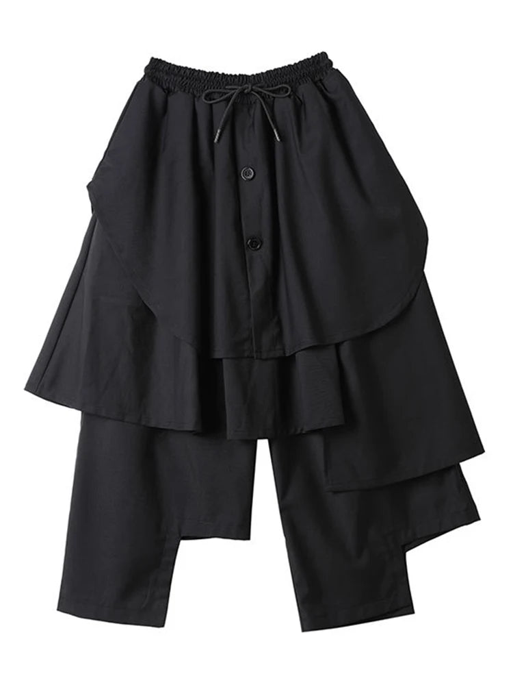 Black cropped wide-leg pants with layered asymmetric panels, buttons, and a drawstring waist, product view.