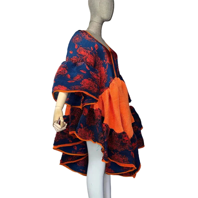 Side view of a navy, red, and orange pleated dress with puffed sleeves and an irregular hem on a mannequin.
