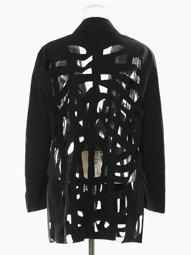 Back view of a black blazer with geometric cutouts and solid long sleeves on a clear mannequin.