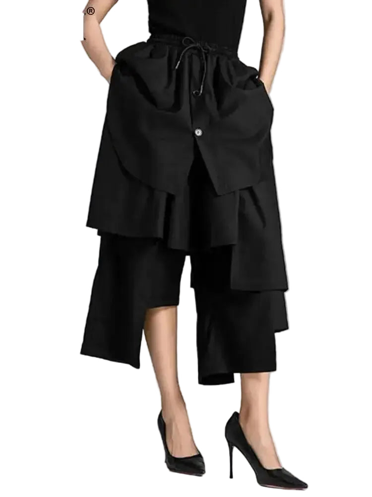 Model wearing black cropped wide-leg pants with tiered asymmetric panels and a drawstring waist, front view.