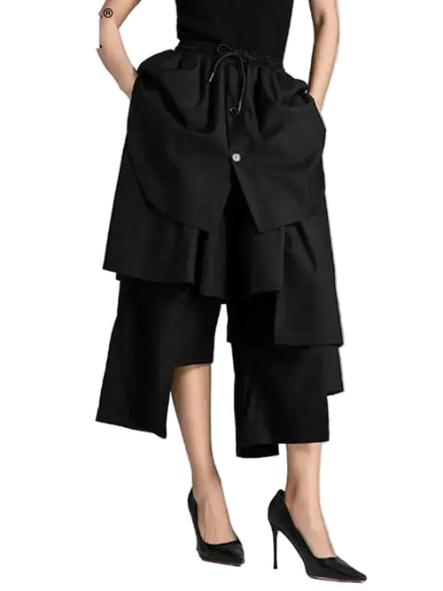 Model wearing black cropped wide-leg pants with tiered asymmetric panels and a drawstring waist, front view.