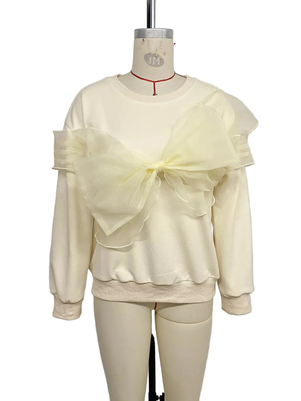 Cream crewneck sweatshirt with an oversized sheer bow and layered shoulder ruffles on a mannequin, front view.