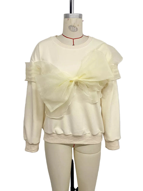 Cream crewneck sweatshirt with an oversized sheer bow and layered shoulder ruffles on a mannequin, front view.