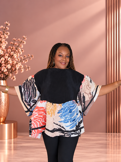Model wearing a pleated black and multicolor floral-print top with wide sleeves, front view.