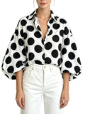 Model wearing a white collared button-front shirt with large black polka dots and puff sleeves, front view.