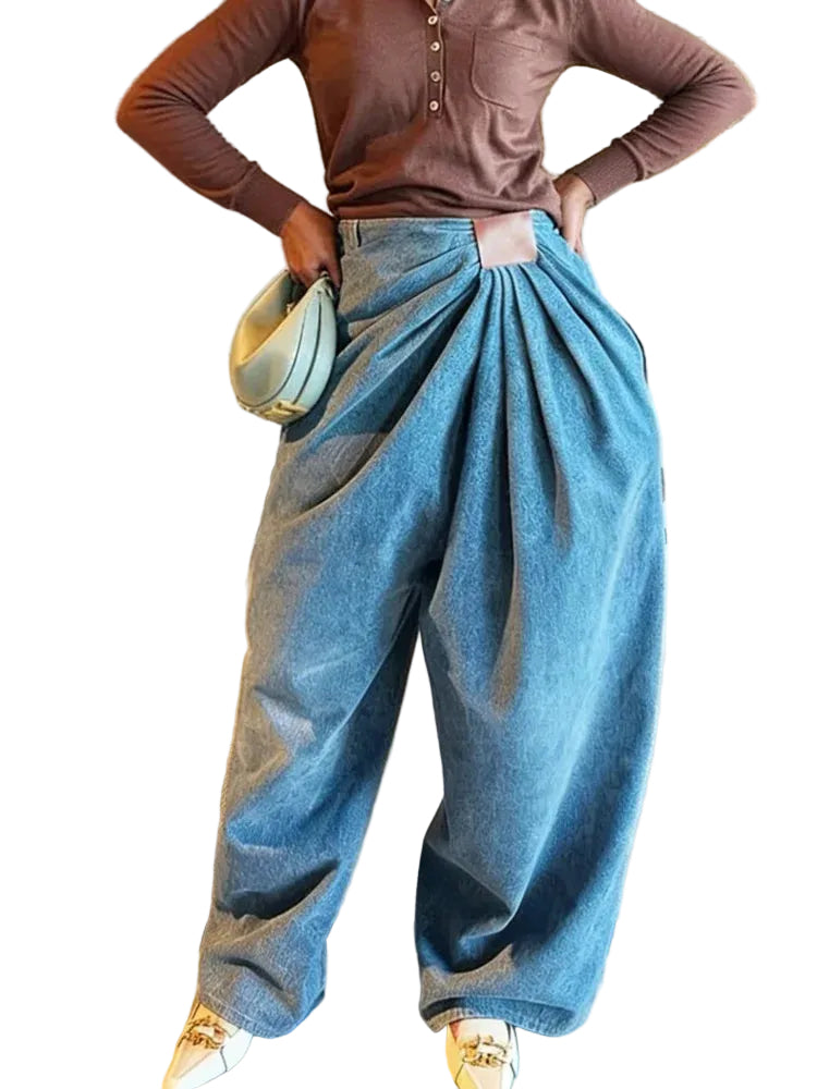 Model wearing blue wide-leg jeans with gathered diagonal pleats and a rectangular brown waist patch, front view.