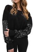 Model wearing a black boat-neck blouse with sequined lower sleeves and black cuffs, front view.