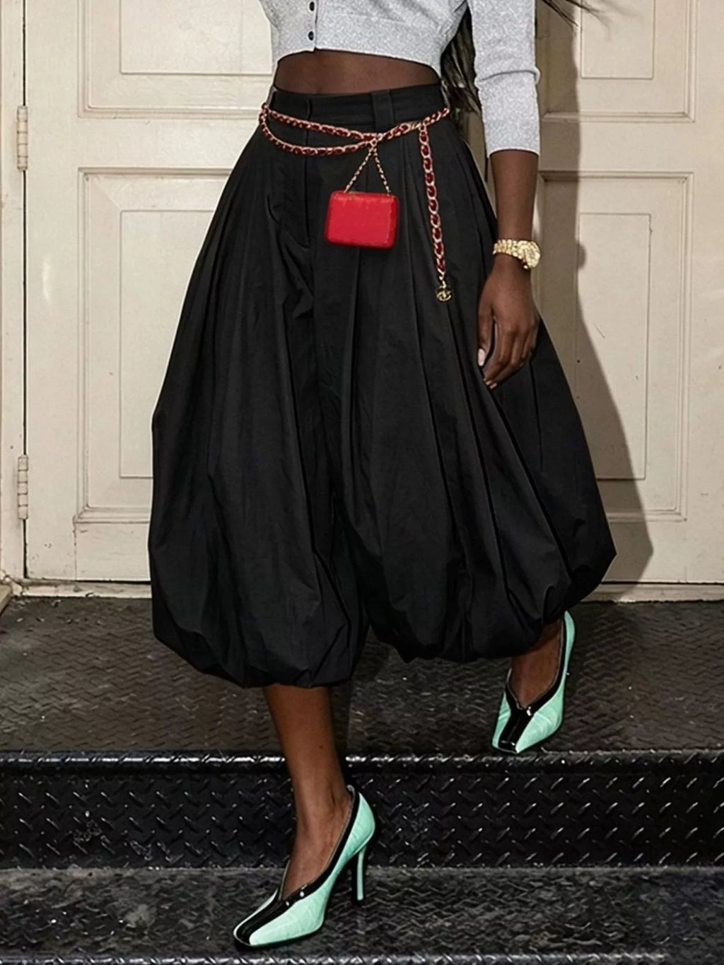 Model wearing black high-waist balloon pants with pleats and gathered hems, styled with a chain belt.