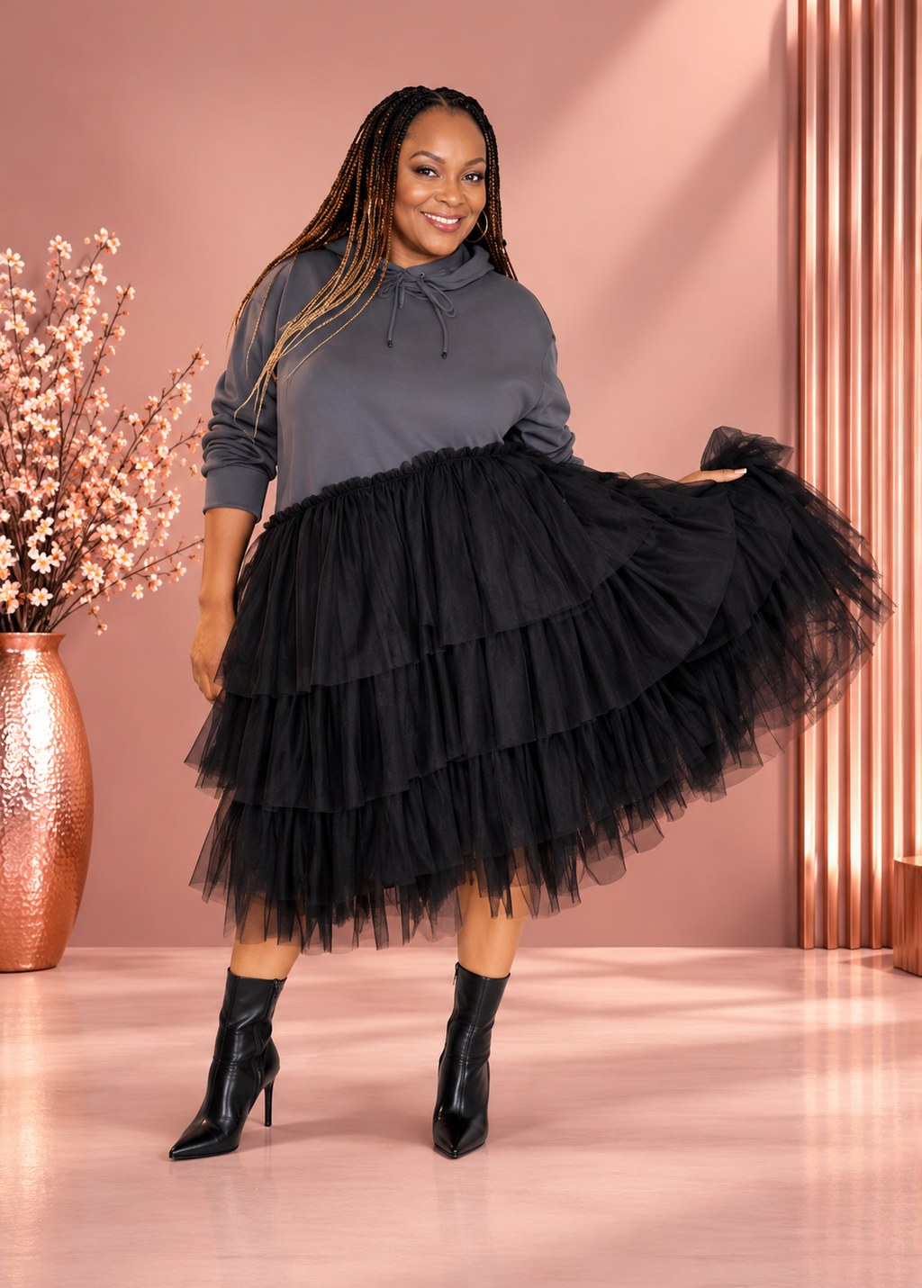 Model wearing a gray hooded dress with a black tiered tulle skirt, lifting the skirt outward.