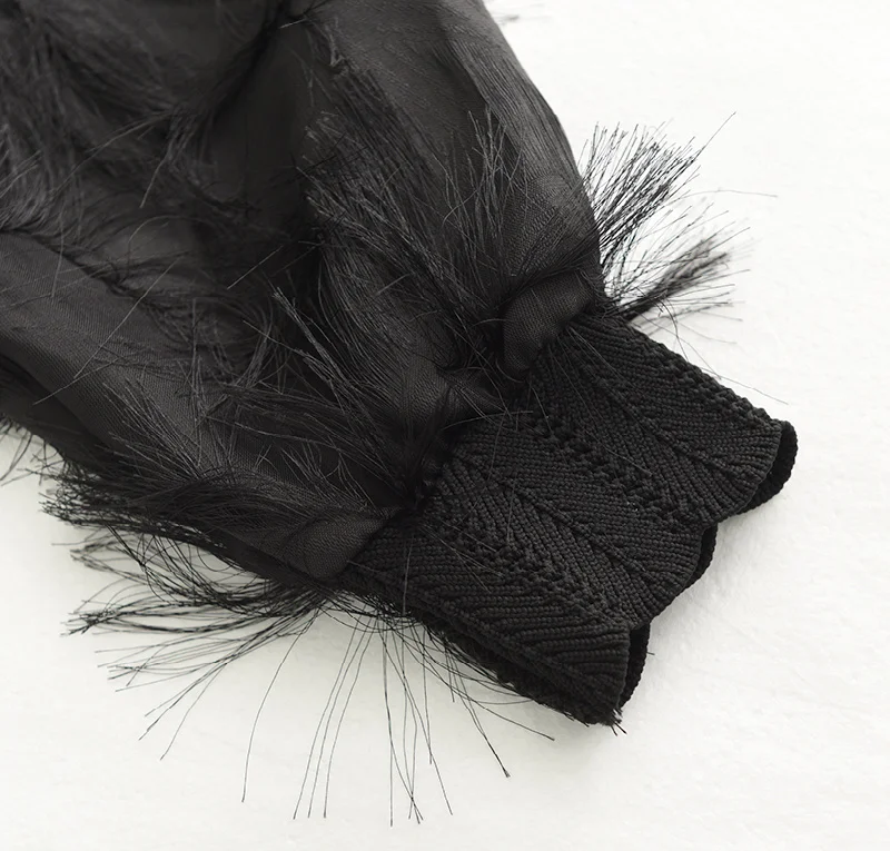 Close-up of a black dress sleeve with sheer fringe fabric and a scalloped textured cuff.